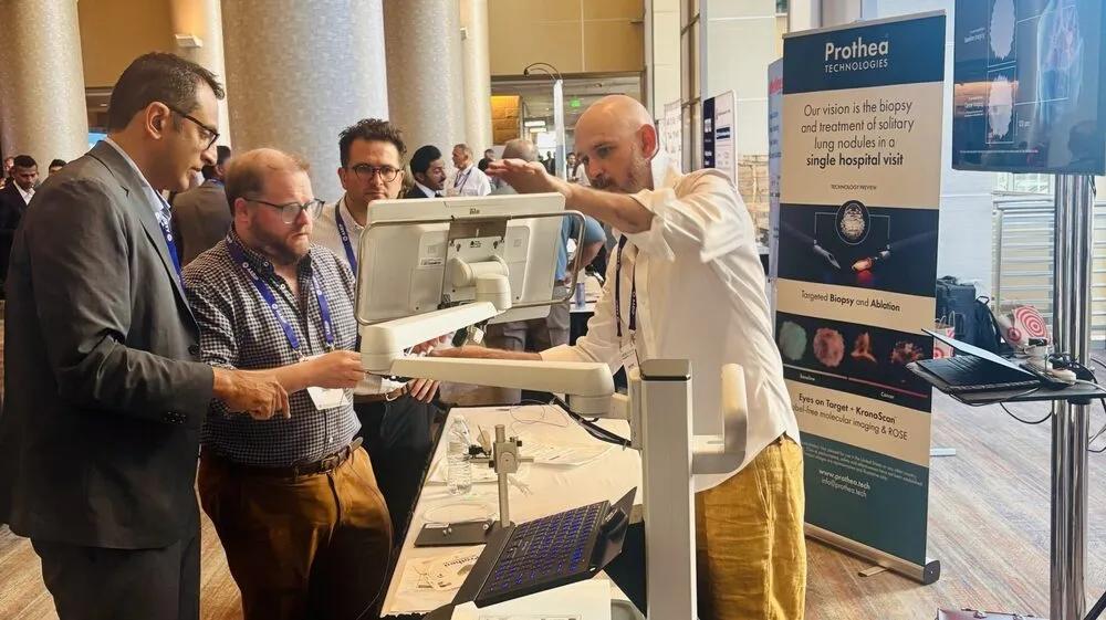 Members of Prothea are standing in discussion, whilst looking at a screen at a conference stall
