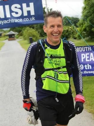 Stephen Gordon participating in the Three Peaks Yacht Race. He is smiling in running gear and wearing a backpack.