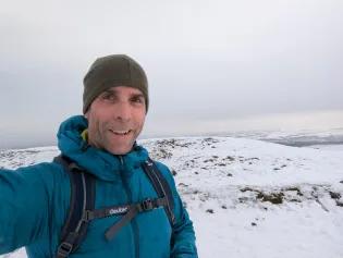 Headshot of Steve at the top of a snowy mountain with hat 