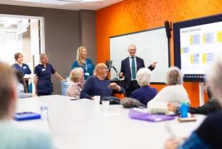 Boardroom with Adam Hill presenting to a room, and patients and nurses are there