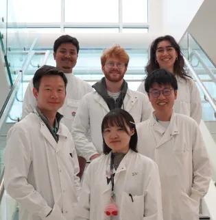 Wei-Yu Lu and is five lab members smiling in the internal IRR staircase in the lab, with their lab coats