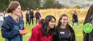 three students laughing outside wearing coats. oen holds a sports cone and another a fishing net