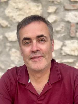 Professor Donal O'Carroll is smiling at the camera, wearing a red shirt in front of a stone wall
