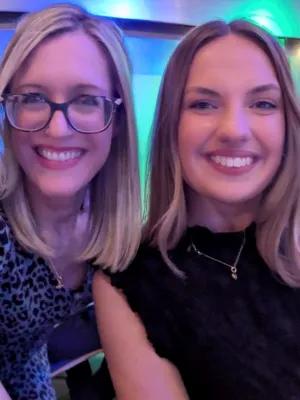 Kathleen and Emma are smiling at the camera with purple and blue lighting behind them