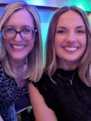 Kathleen and Emma are smiling at the camera with purple and blue lighting behind them