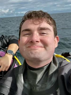 Alex smiling on a boat in a scuba outfit