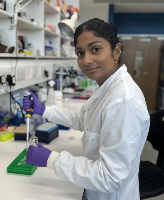 Roseanne Rosario wearing lab coat and gloves in a lab, pipetting liquid into a vial.