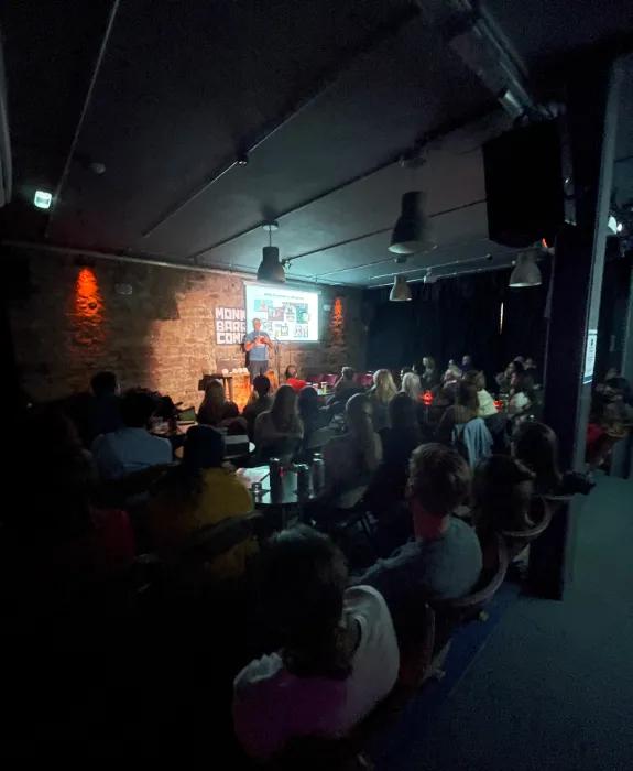 Rob Illingworth on a stage presenting to a large audience in a darkened room 
